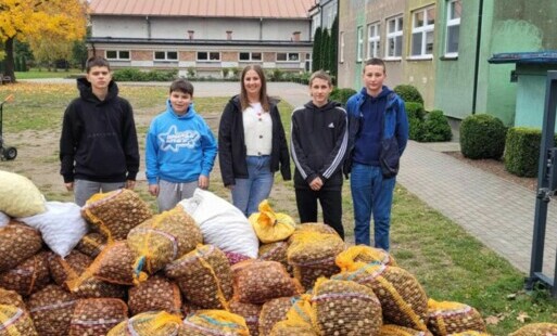 Grupa dzieci stoi przez duża ilością siatkowych worków z kasztanami